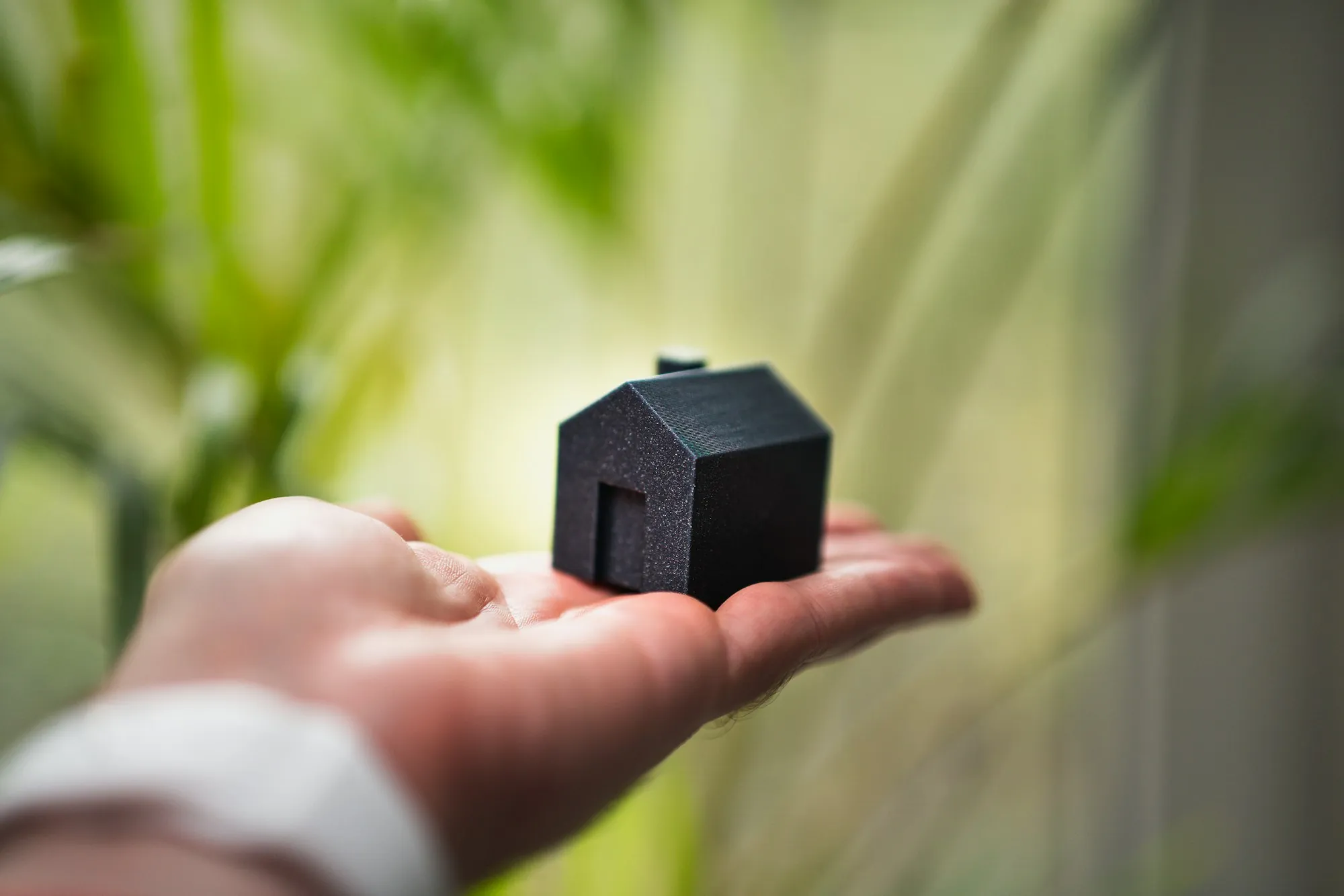 Hand holding a small black model house against a green background